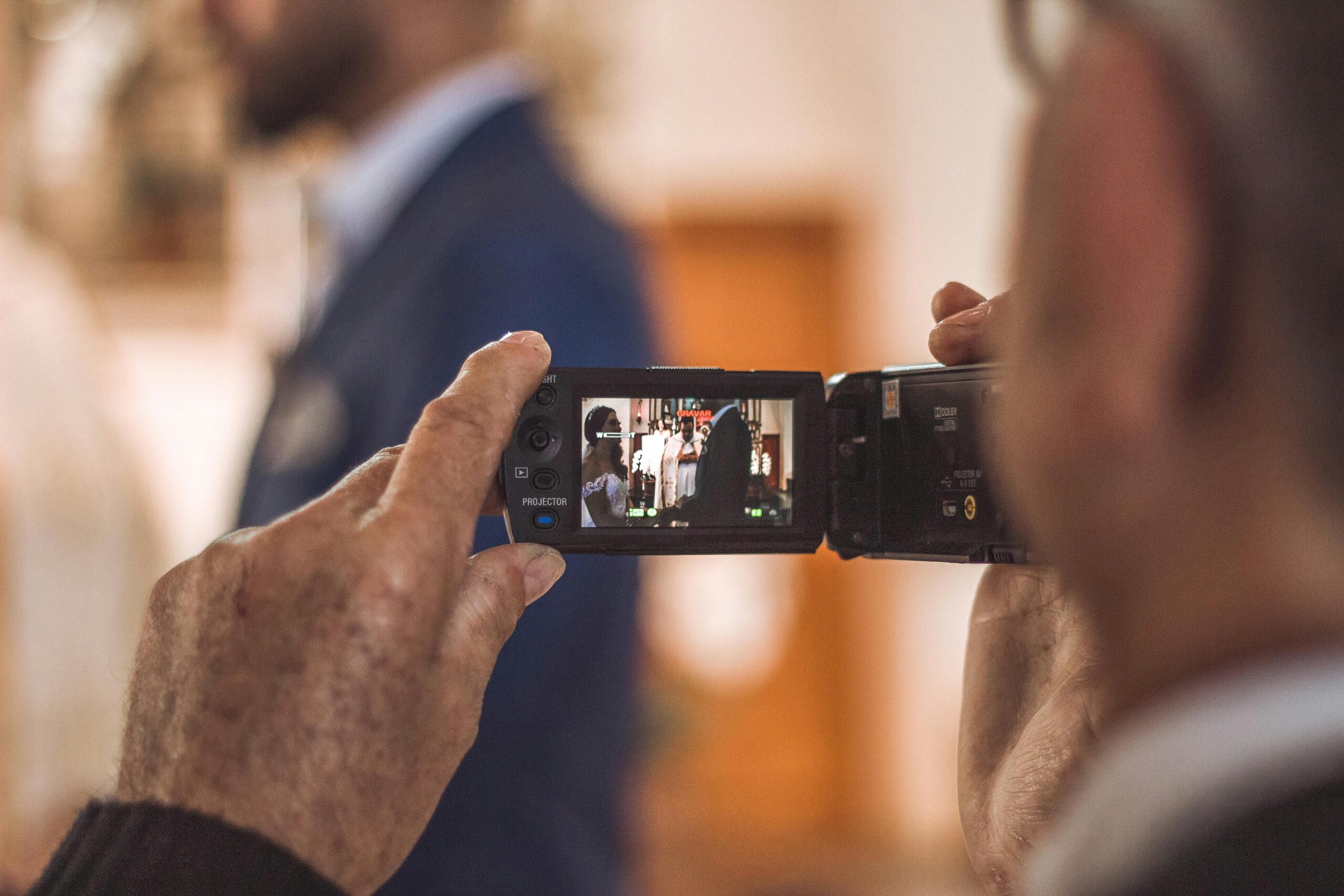Hands holding camcorder filming a wedding ceremony